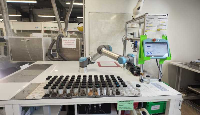 Robotic laboratory arm handling rows of soil sample jars at an automated testing station