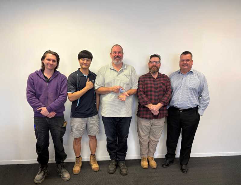 Five team members standing together, with one holding a small recognition award