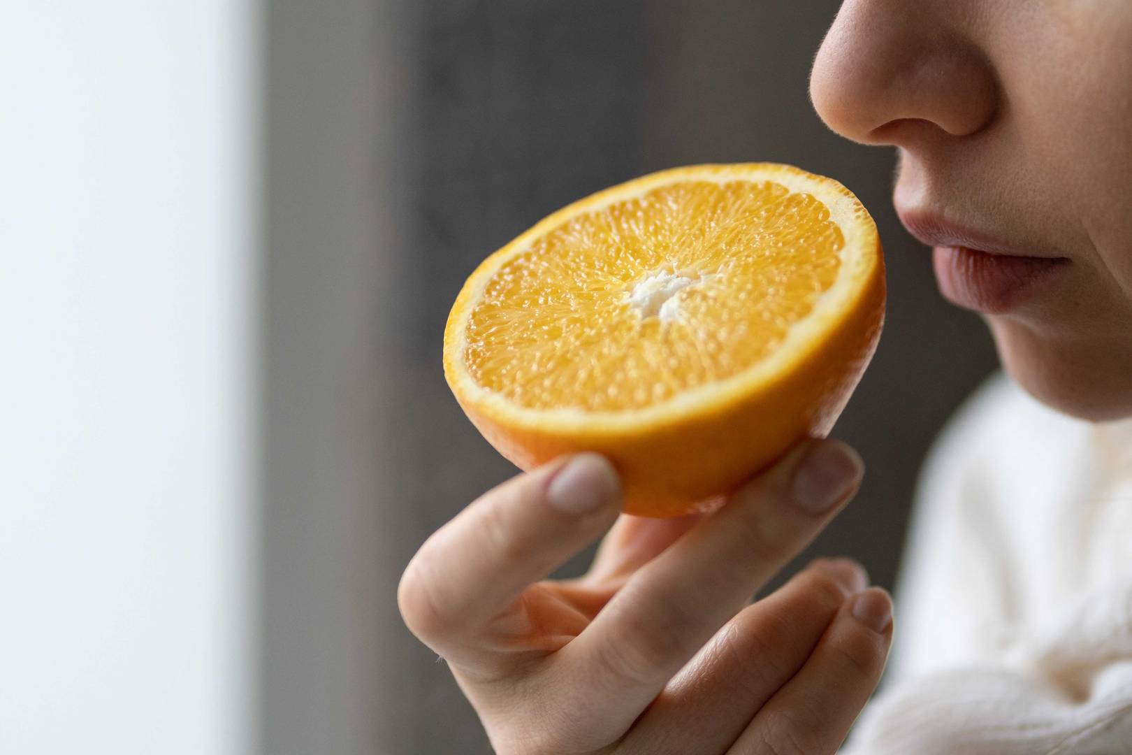 Woman smelling a half cut orange fruit