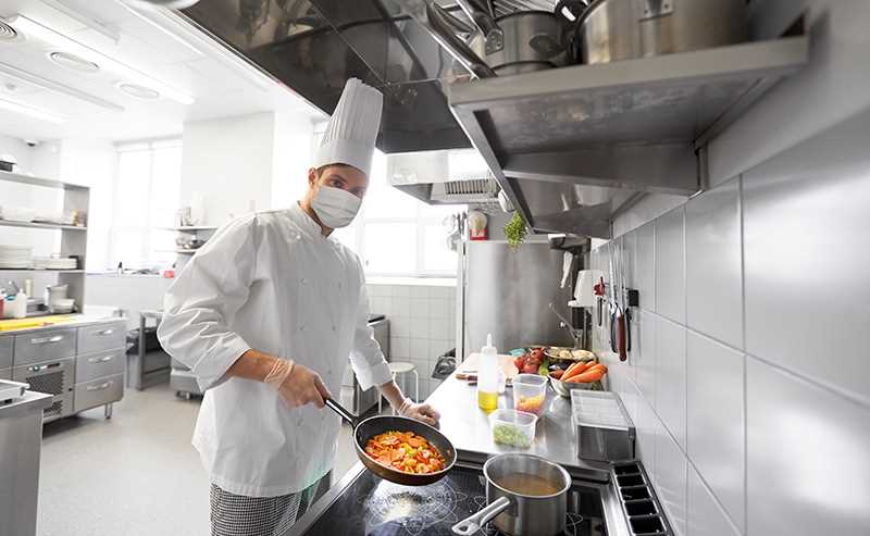 Chef cooking food in a professional kitchen, flipping ingredients in a pan.