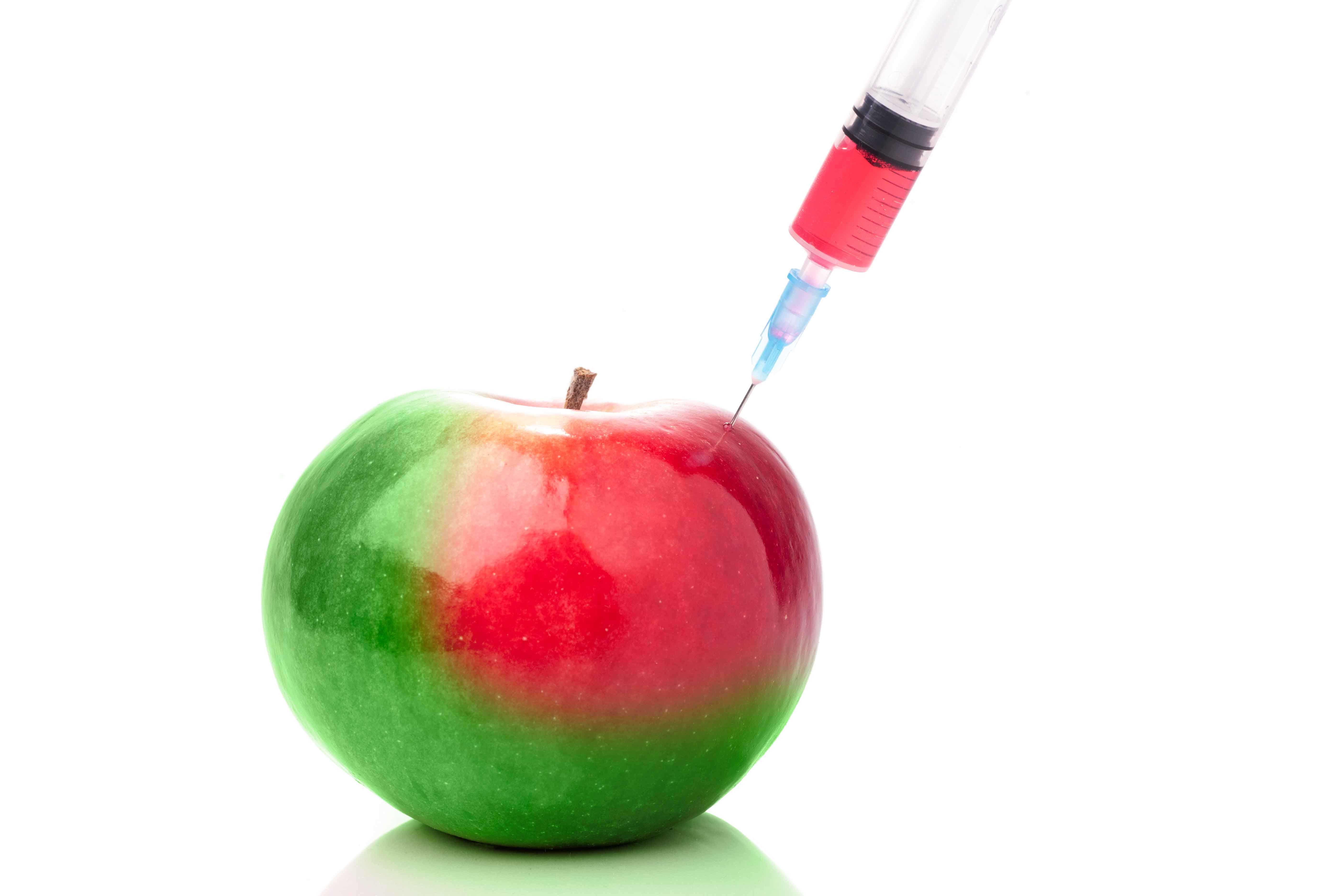 Maçã verde a ser injetada com líquido vermelho por uma seringa.