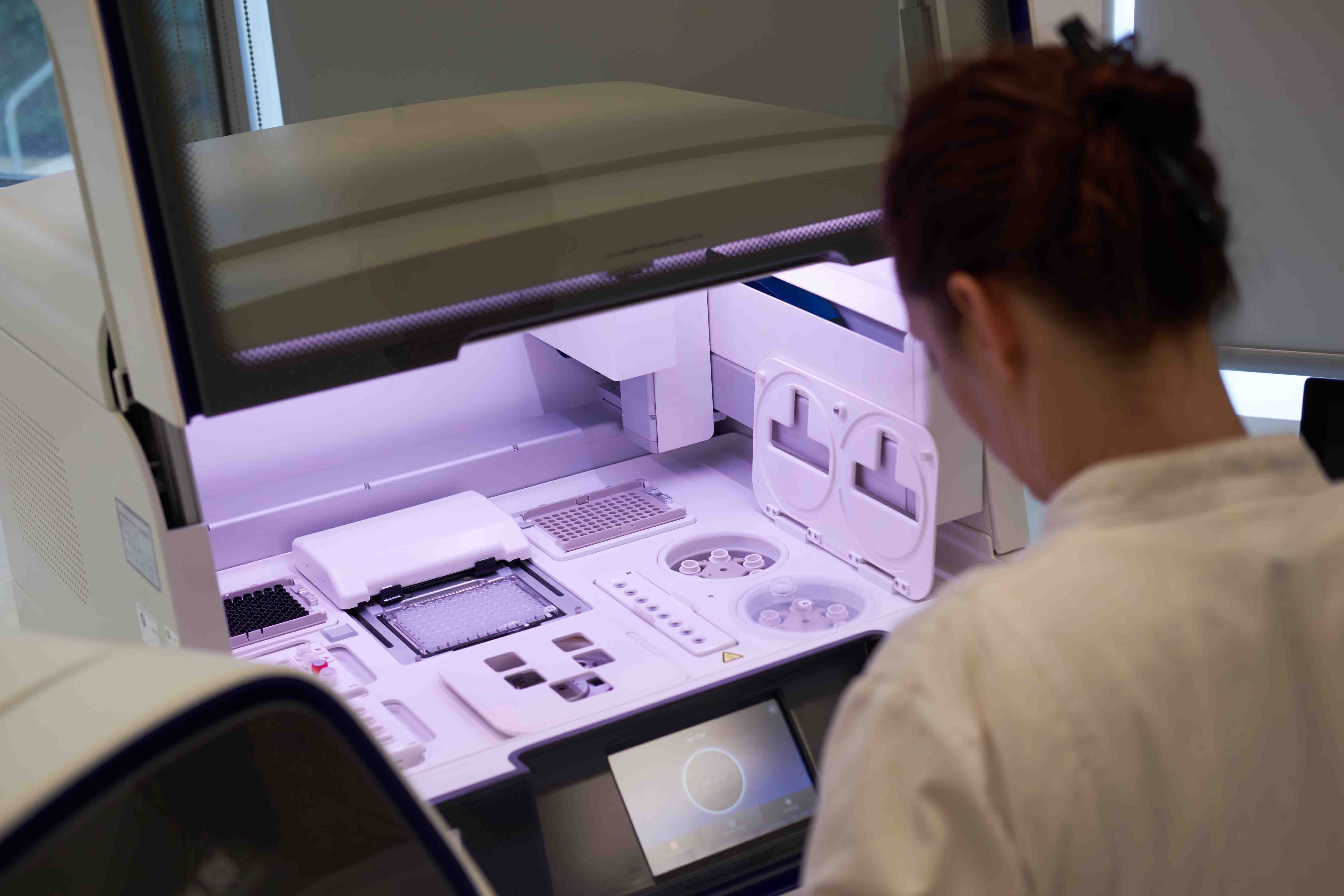  Técnico de laboratório a utilizar equipamento avançado com interface tátil e compartimentos múltiplos.