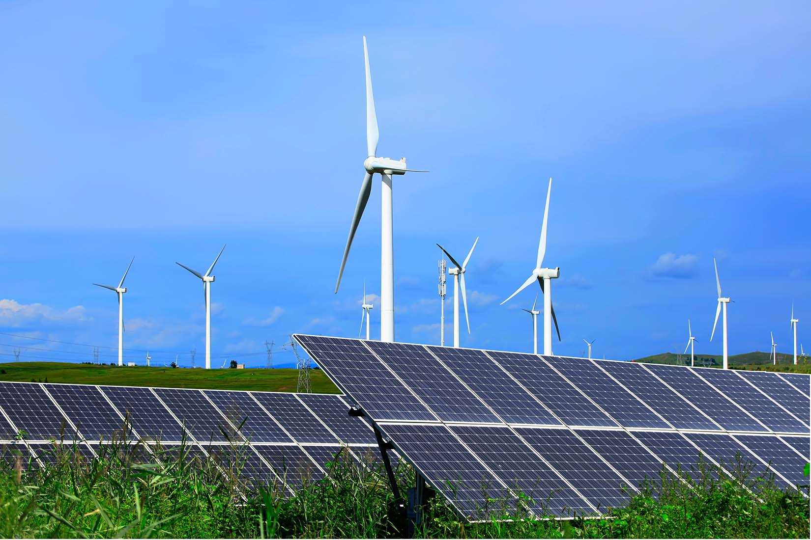 Paisagem com turbinas eólicas e painéis solares sob céu azul claro, representando fontes de energia renovável e tecnologias sustentáveis.