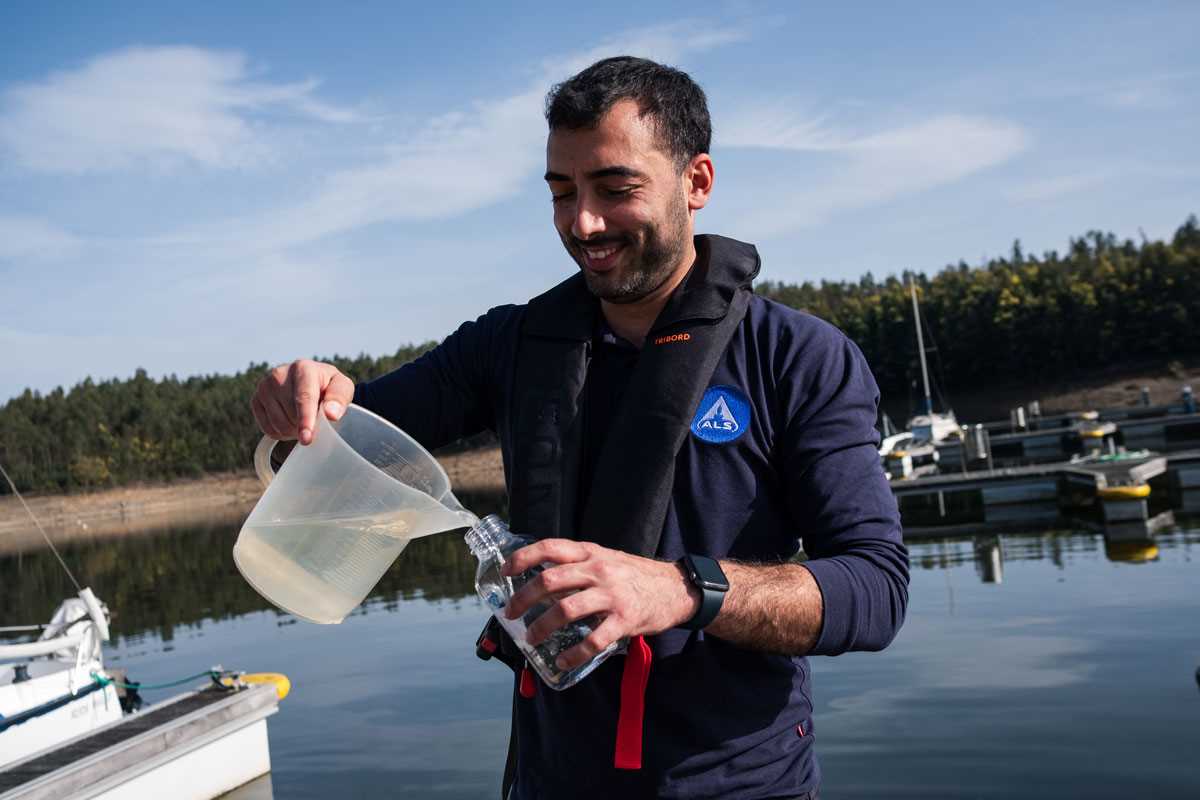 Técnico a transferir amostra de água de um jarro para um frasco durante recolha de amostras junto a uma zona de marina.