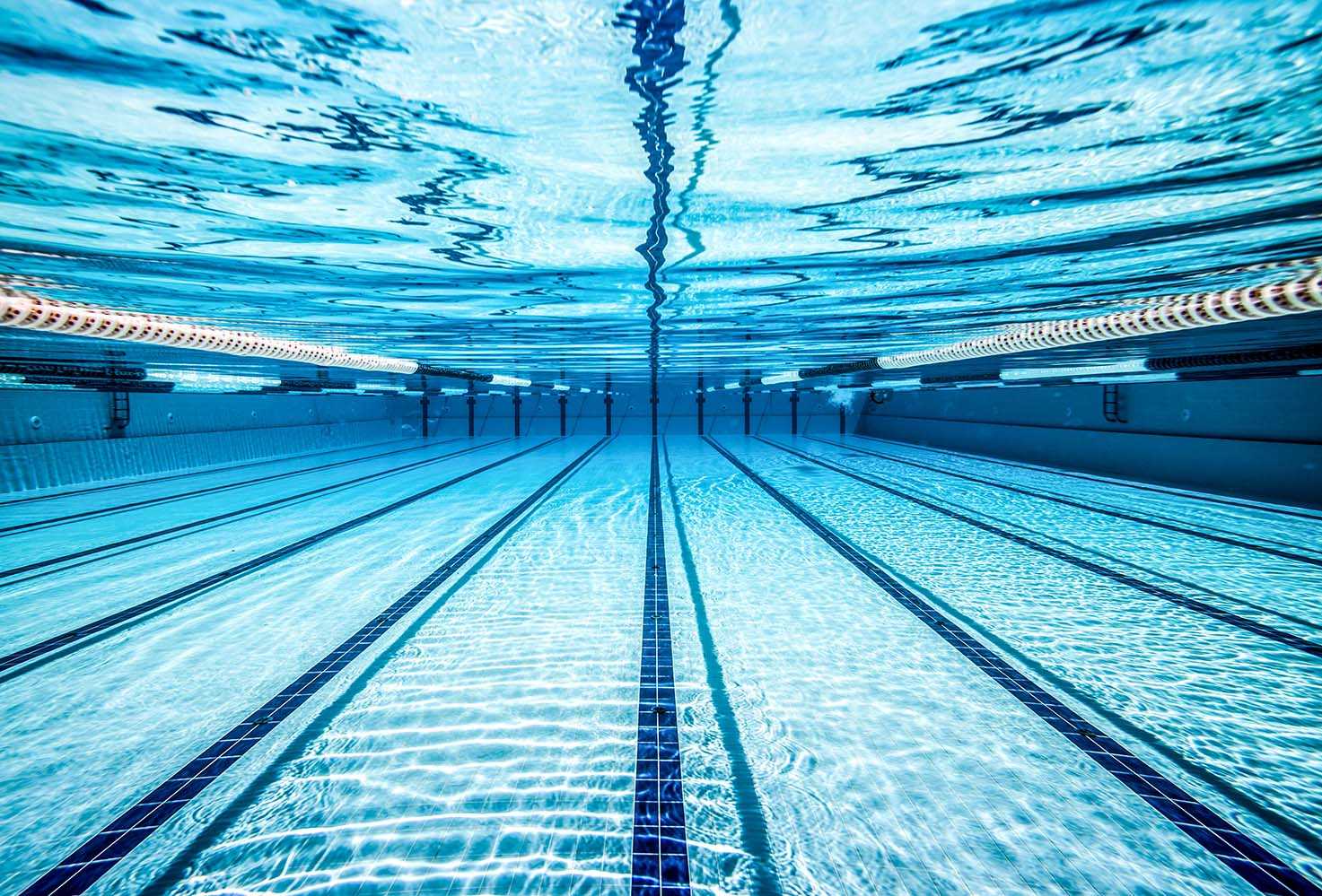 Vista subaquática de uma piscina com várias pistas, água cristalina e marcações visíveis no fundo.