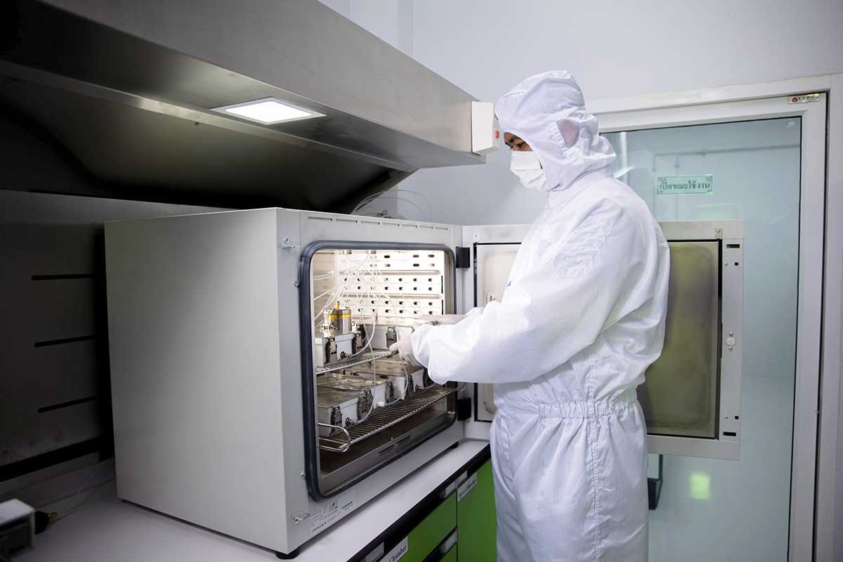 A person wearing cleanroom protective clothing places samples inside an open laboratory thermal desorption or GC‑MS test chamber under a ventilation hood in a controlled laboratory environment.