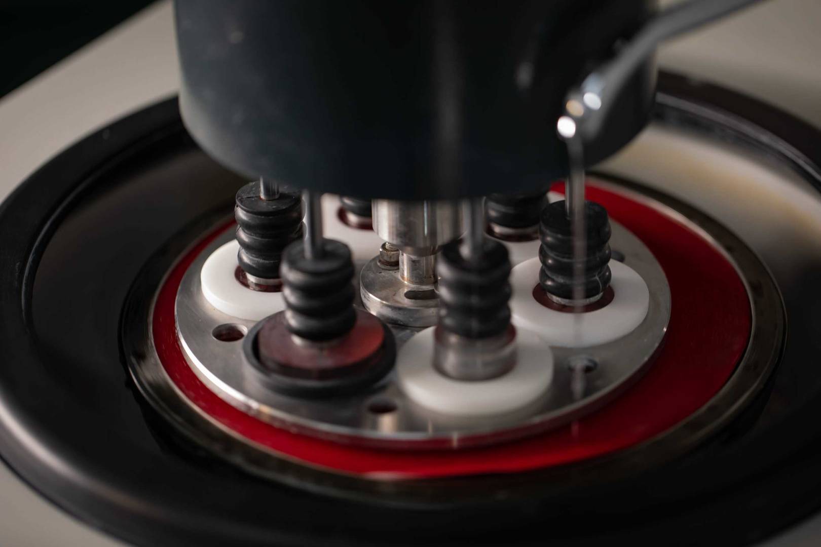 Close‑up view of a micro‑sectioning or polishing machine head pressing multiple sample mounts in a circular holder during laboratory material testing.