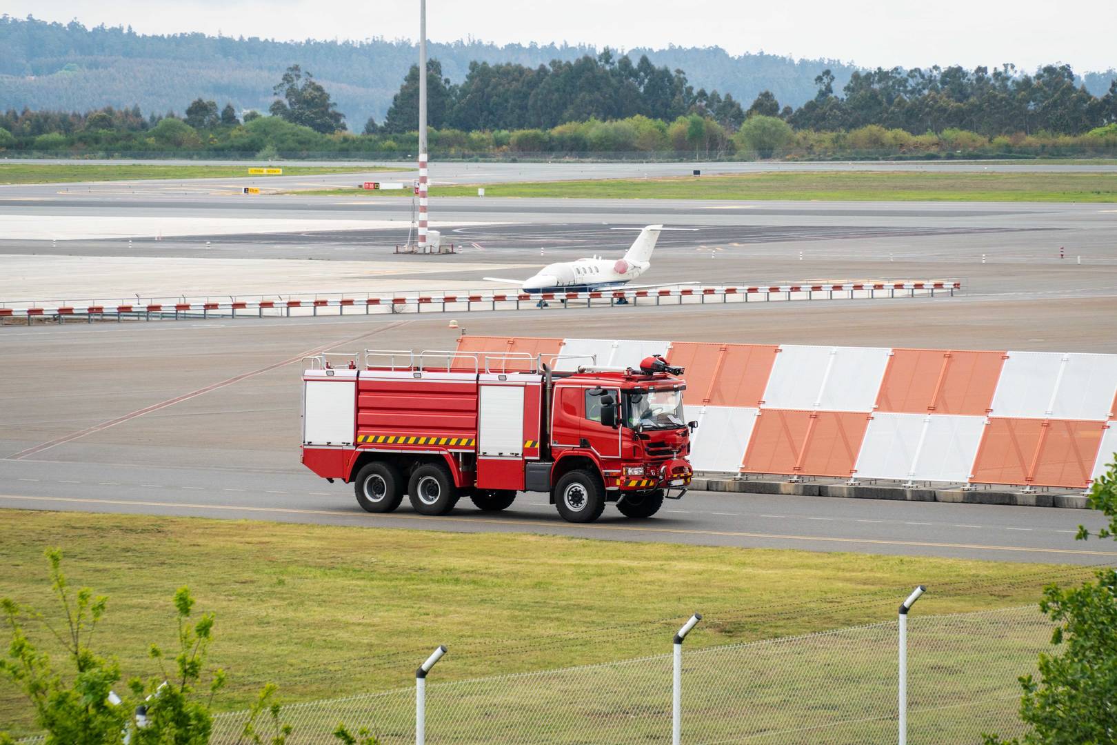 a fire engine at an airport, with a small plane in background