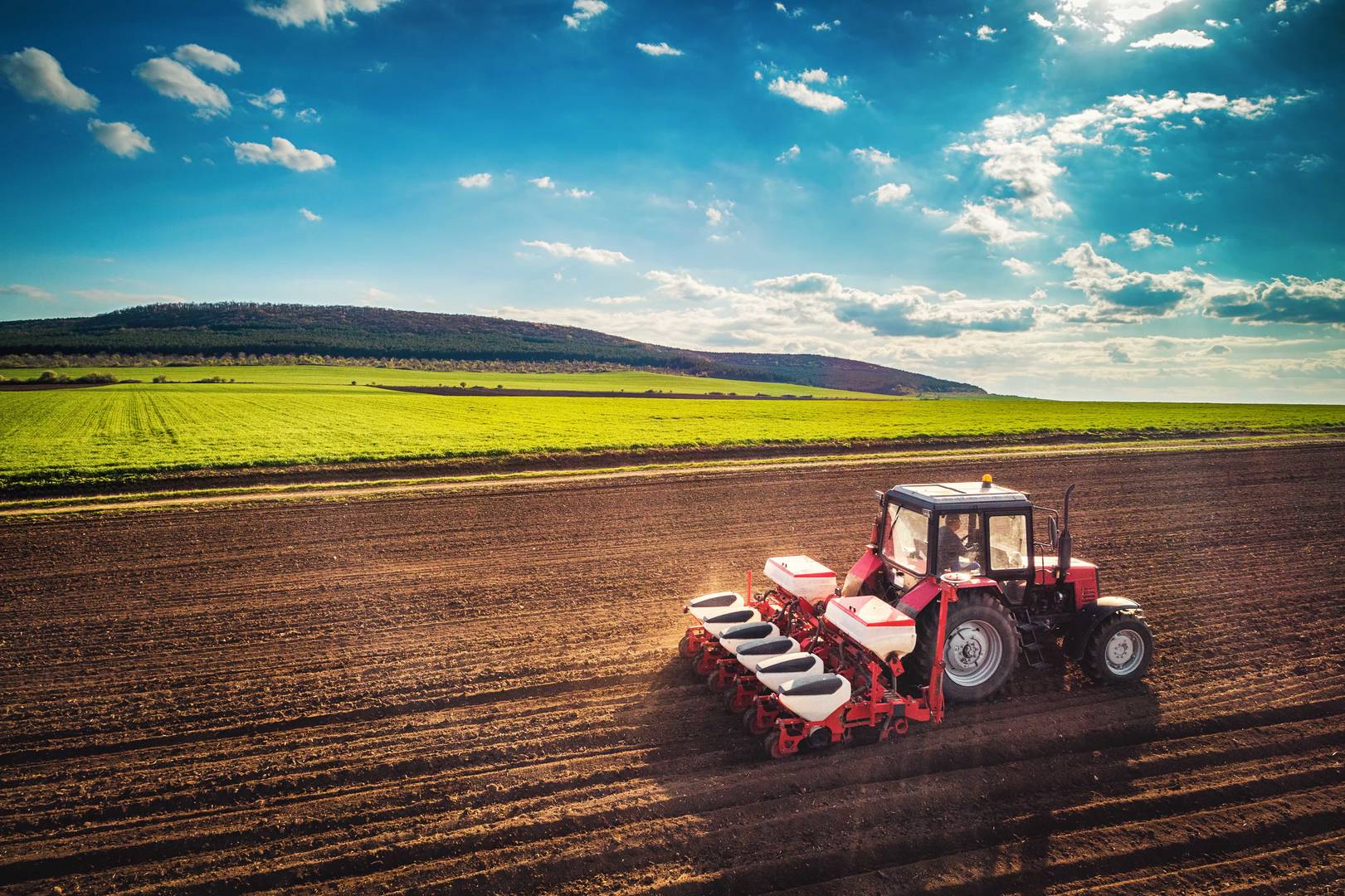 a red tractor ploughing a field in front of green hills