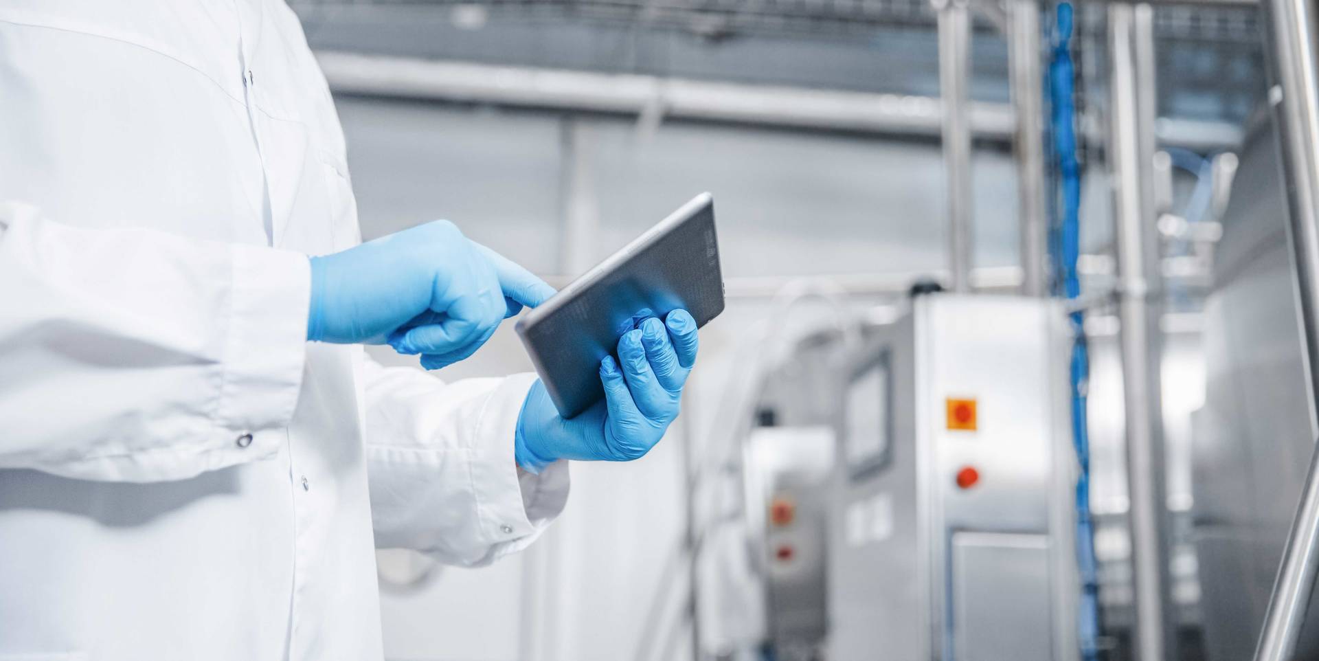Person med labfrakk holder tablet i produksjonsområdet