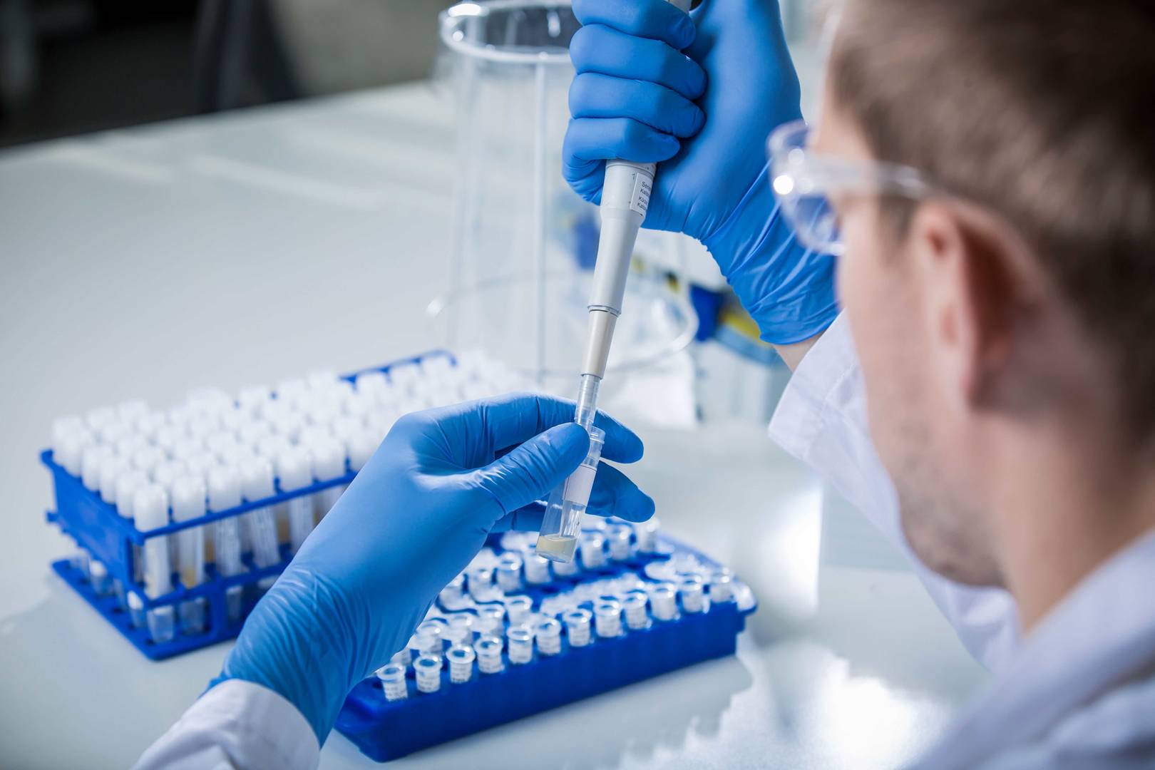 A scientist in a laboratory using a pipette to handle liquid samples, surrounded by laboratory equipment